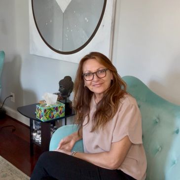 Woman with glasses sitting on a teal chair.