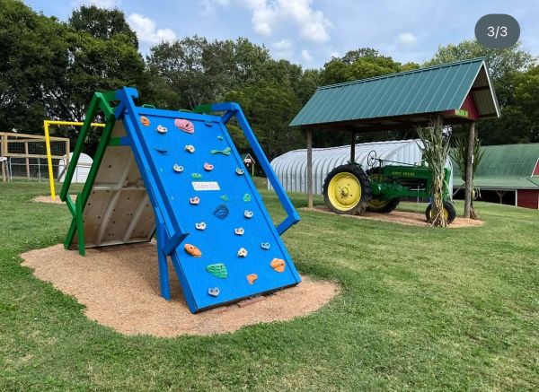 Outdoor playground with climbing wall and tractor under metal roof.