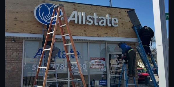 Workers installing or repairing an Allstate sign on a building.