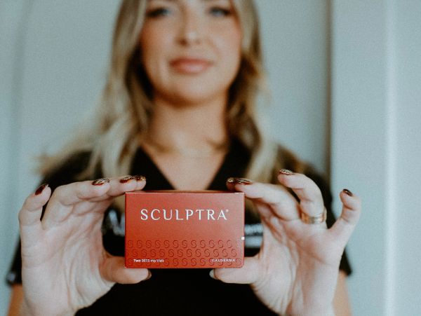 Person holding a red Sculptra product box with both hands.