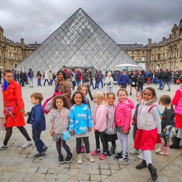 Kids in front of the pyramid of the Louvre with a tour guide in Paris