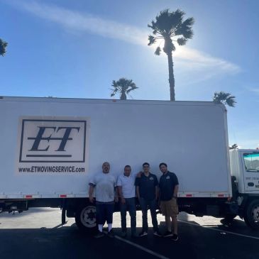 Four men standing in front of a moving service truck under a sunny sky.