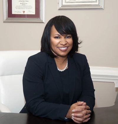 Smiling woman in a black blazer sitting at a desk.