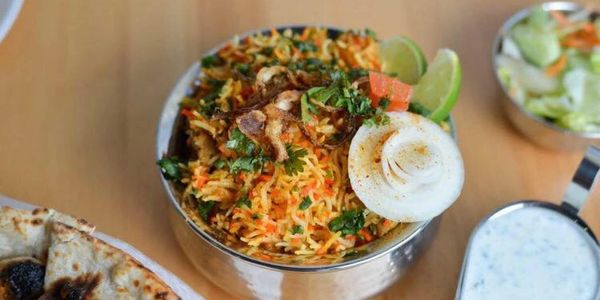 A bowl of flavorful biryani with garnished onion and lime, served with naan and raita.