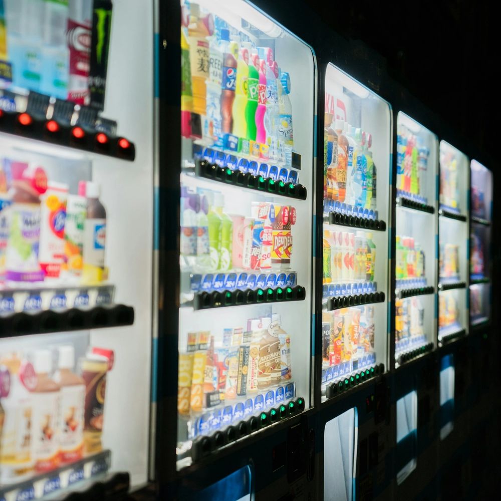 Row of illuminated vending machines stocked with colorful drinks at night.