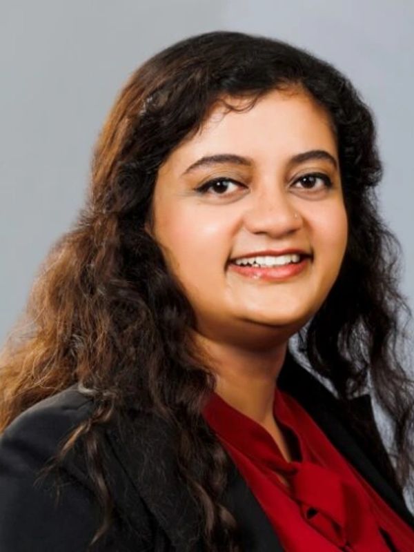 Smiling woman with long curly hair in a red top and black jacket.