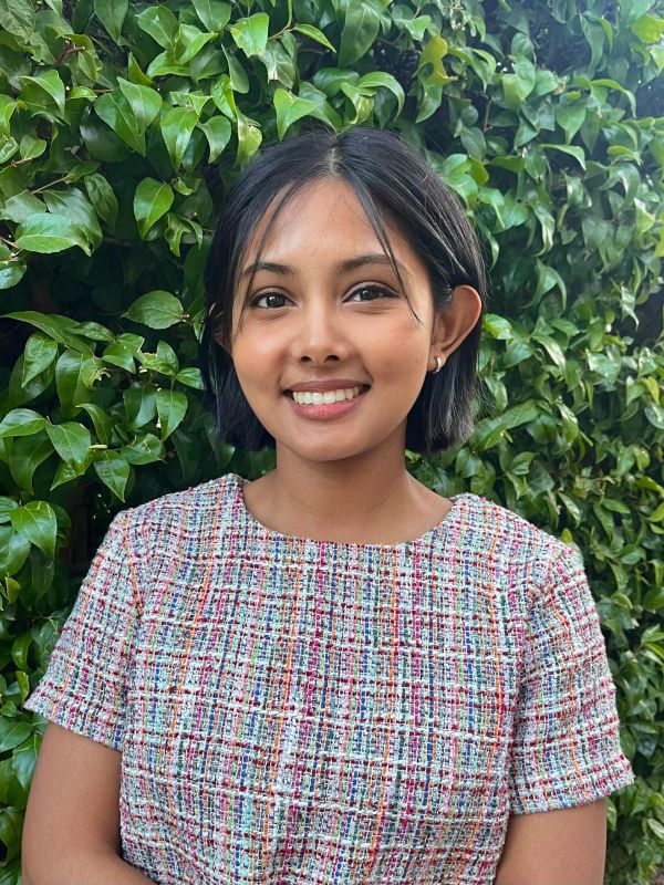 Smiling young woman with short hair in front of green leaves.