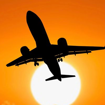 Silhouette of an airplane flying against a vibrant orange sunset.