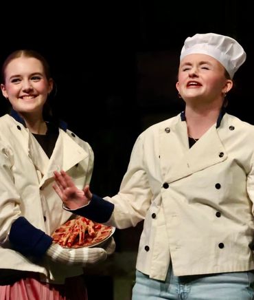 Two young actors in chef costumes performing on stage.