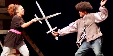 Two actors sword fighting on stage in a dramatic scene.