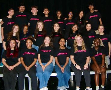 A diverse group of young theatre performers posing together in matching black t-shirts.