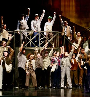 Cast performing a powerful, unified scene with raised fists on stage.