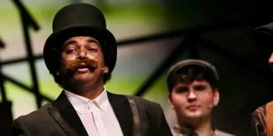 Man in a top hat and glasses with a mustache during a performance.