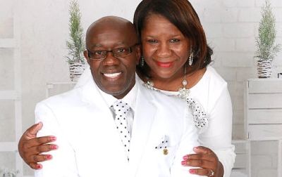 A smiling couple dressed in white posing together indoors.