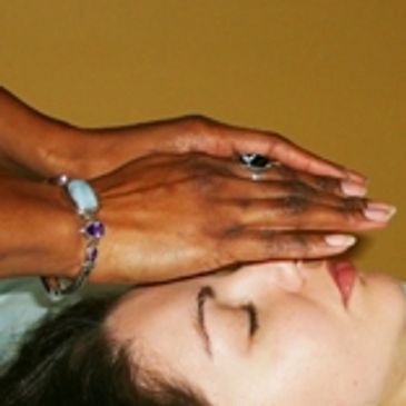 Hands performing a healing or relaxation touch on a person's forehead.