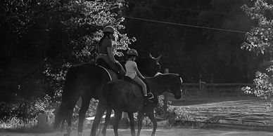 Two people riding horses in a wooded area.