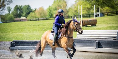 A person riding a horse through water in an outdoor setting.
