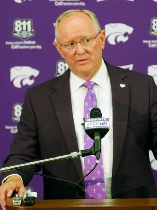 Man in suit speaking at a podium with purple backdrop.