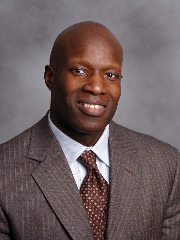 Man in a brown suit smiling at the camera.