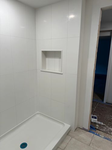 Newly renovated white tiled shower corner with built-in shelf.