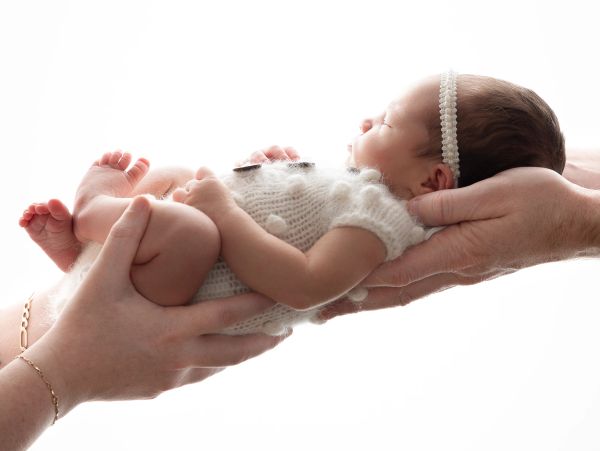Newborn baby held gently by adult hands.