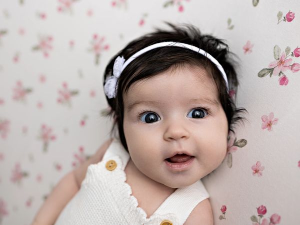 Adorable baby girl with dark hair and a white headband.