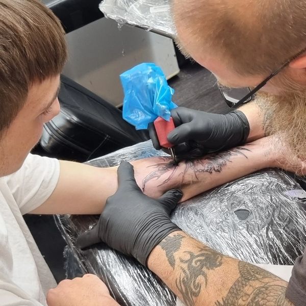Tattoo artist inking a design on a client's forearm in a studio.