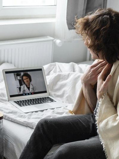 A person wrapped in a blanket having a video call with a doctor on a laptop.