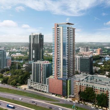 Modern skyscraper amidst urban landscape with highway in foreground.