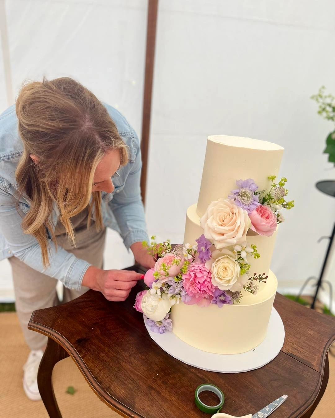 Woman decorating a three-tiered cake with flowers.