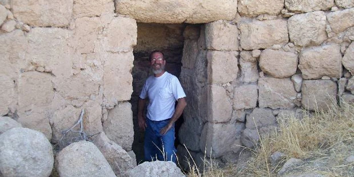 Man standing in a small stone doorway of an ancient ruin.