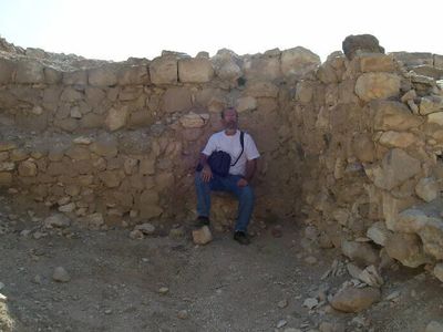 A man sitting inside an ancient stone structure amid desert surroundings.