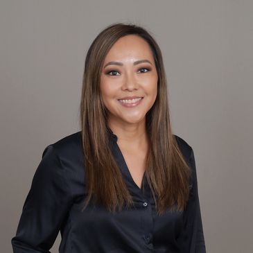 Smiling woman with long hair wearing a black blouse against a neutral background.