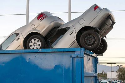 Two cars stacked unusually in a large blue dumpster outdoors. Cash for cars red oak tx
