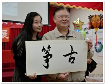 Two people holding a board with Chinese calligraphy characters.