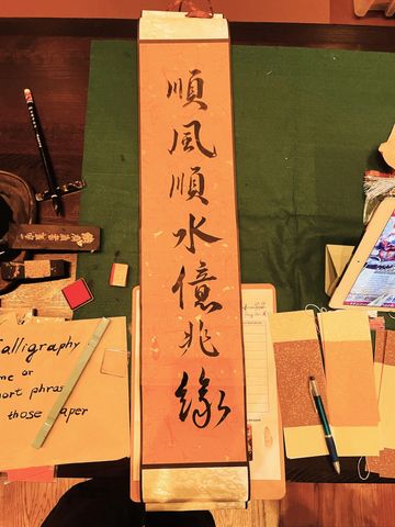 A traditional calligraphy scroll with Chinese characters on a table surrounded by writing tools.