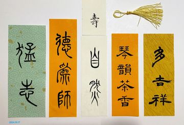 Five vertical paper strips with Chinese calligraphy and a tassel on a white background.