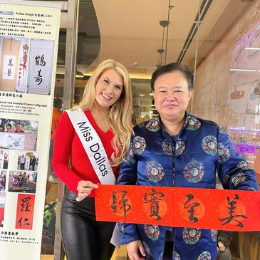 Miss Dallas posing with a man holding a red calligraphy scroll.
