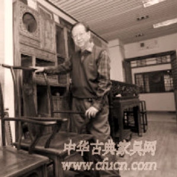 Elderly man posing with antique wooden furniture in a traditional room.
