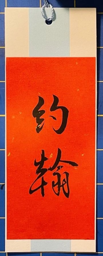 Red paper with black Chinese calligraphy characters on a hanging scroll.