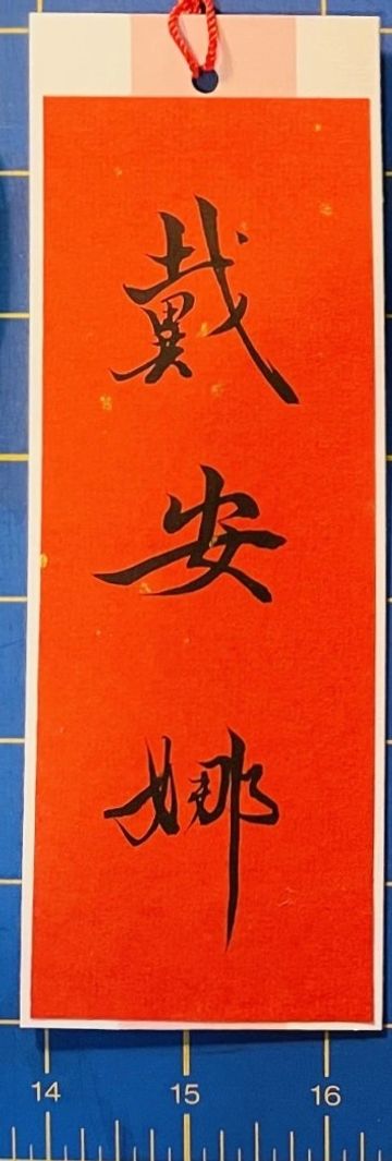 Red paper with black Chinese calligraphy characters and a red hanging cord.
