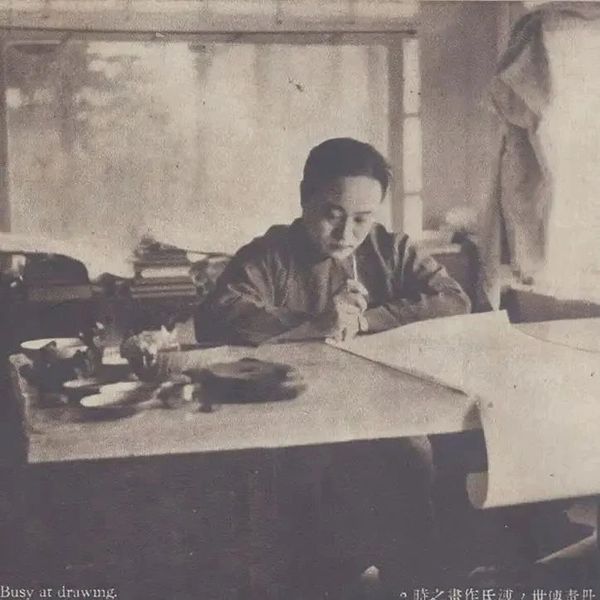A man focused on drawing at a cluttered desk in a dimly lit room.