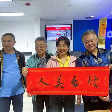 Four people holding a red banner with Chinese calligraphy indoors.