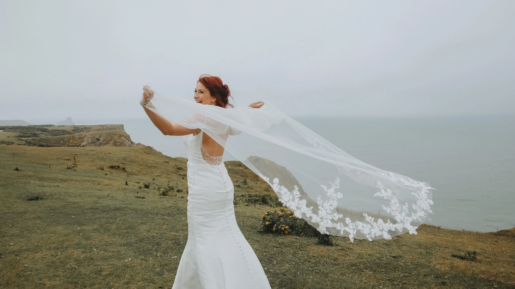 bride with her wedding veil on the cliffs by the sea in wales 
