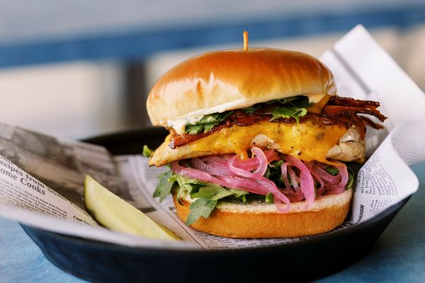 A delicious chicken sandwich with bacon, cheddar, pickled onions, and greens.