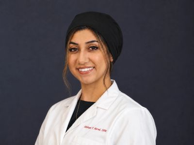 Smiling female medical professional in white coat against a dark background.