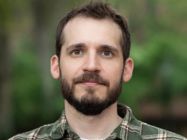 Portrait of a man with a beard and plaid shirt against a blurred green background.