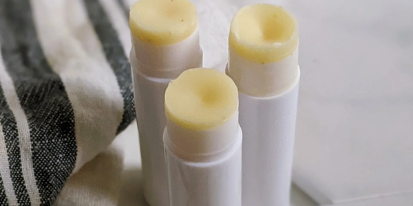 Three tubes of yellowish lip balm on a white surface beside a striped cloth.