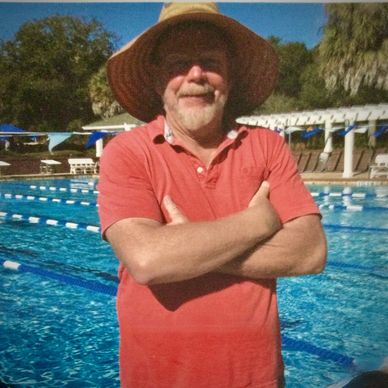Man in red shirt and sun hat at outdoor pool.