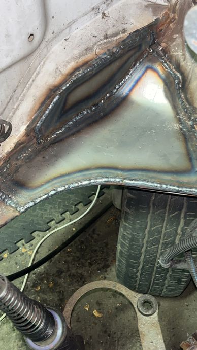 Close-up of a metal surface with fresh welds and a tire in the background.